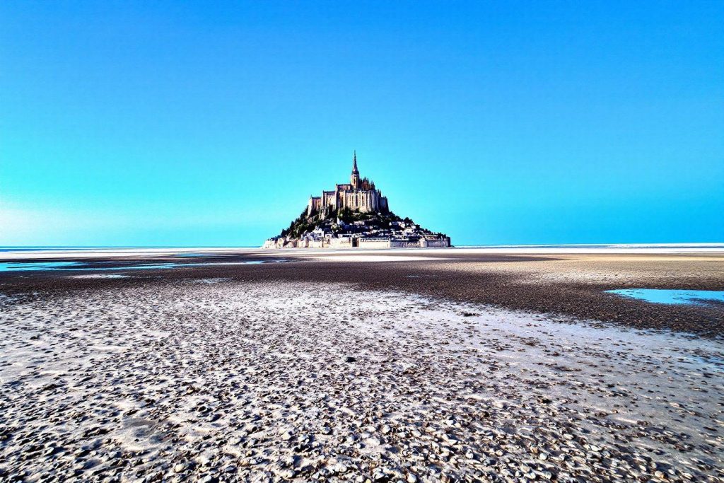 Île abbatiale monumentale émergeant d'une plage rocheuse déserte