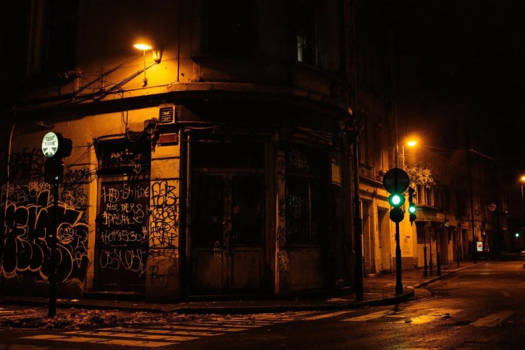 Rue sombre avec lampadaires et graffitis sur mur d'angle