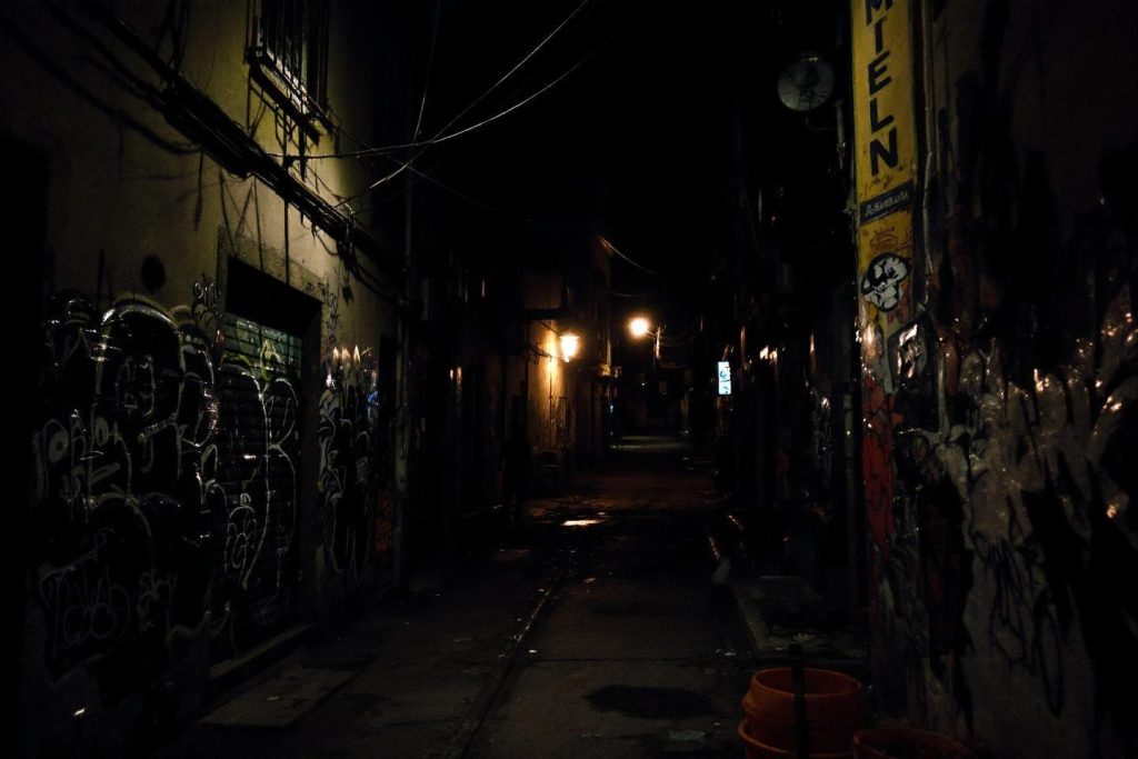 Passage étroit entre murs tagués, éclairé par un lampadaire